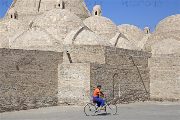 Uzbek man cycling in front of mosque in the ancient historic city of Bukhara