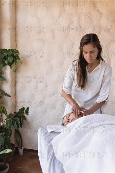 Young woman therapist and female patient having facial massage session massaging at beauty center