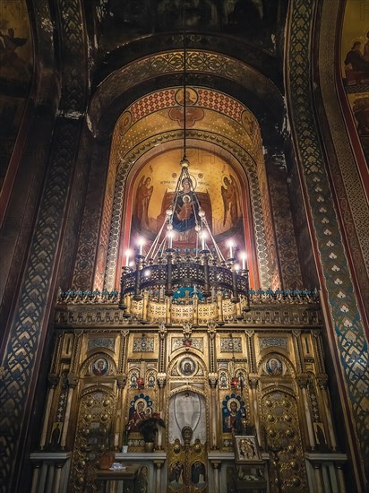 Interior details of Curtea de Arges monastery. The altar and ornate walls with painted icons and a golden chandelier with lights suspending out of ceiling