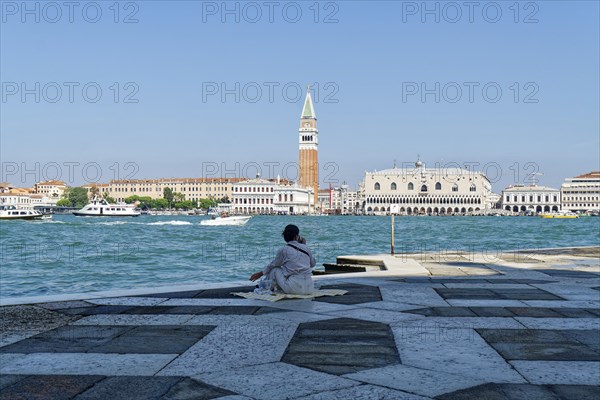 Woman having a picnic in the square in front of the church of San Giorgio Maggiore on the Giudecca Canal with a view of the Doge's Palace