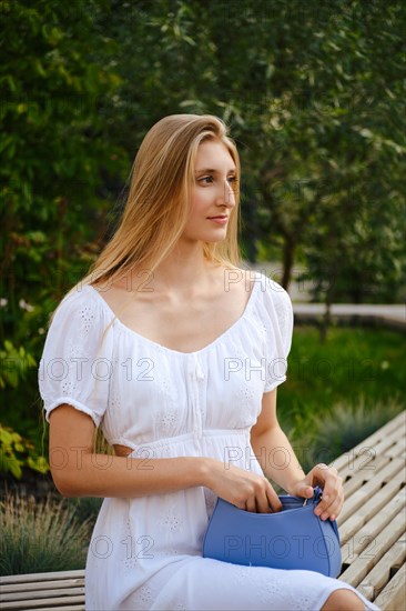 Young woman in white summer dress sitting on a bench waiting for someone