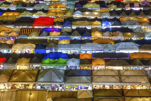 Close-up view of rows of colorful outdoor market tents and food stalls at night. Fairs