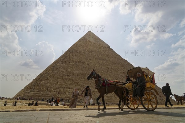 Two-wheeled horse-drawn carriage passes in front of a pyramid