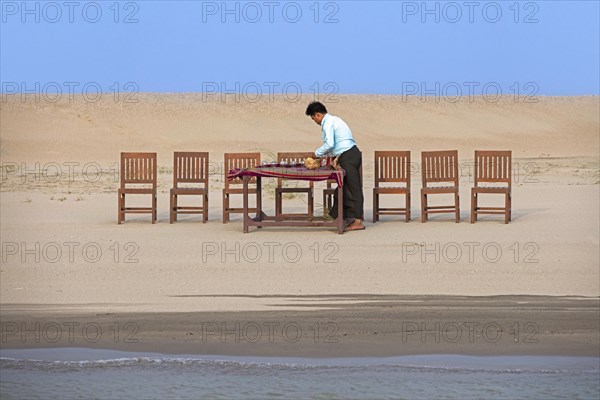 Burmese servant preparing dinner and setting the table for tourists at sunset along the Irrawaddy River
