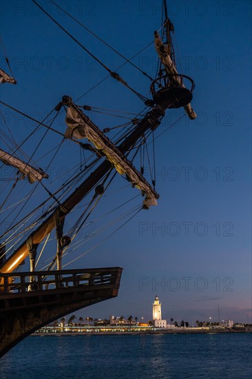 Old ship on the promenade of Muelle Uno in the Malagaport of the city of Malaga and in the background La Farola de Malaga