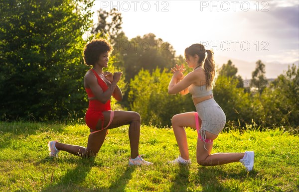 Caucasian blond girl and dark-skinned girl with afro hair doing stretching exercises in a park. Healthy life