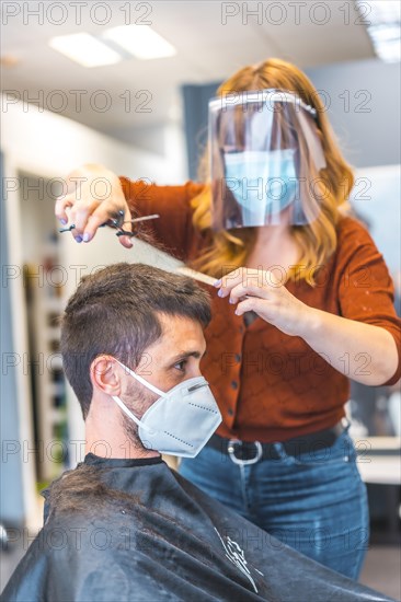 Hairdressers after the Coronavirus pandemic. Caucasian hairdresser with face mask and protective screen