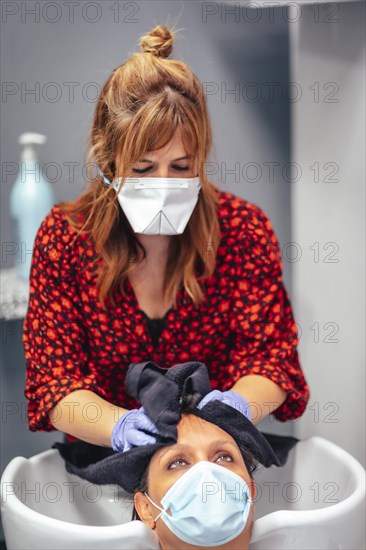 Hairdresser with mask and gloves washing the client's hair with soap and water. Reopening with security measures for hairdressers in the Covid-19 pandemic