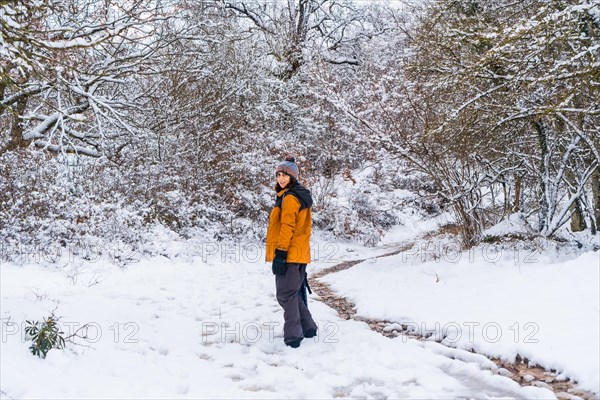 A young woman in a yellow jacket walking along the path of frozen trees. Snow in the town of Opakua near Vitoria in Araba