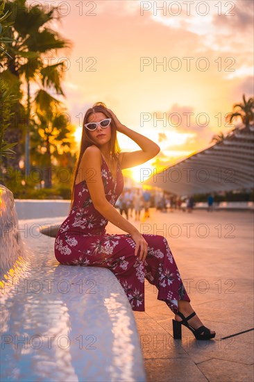 Sunset with a young brunette in a maroon floral dress and modern white sunglasses enjoying the summer in the golden hour