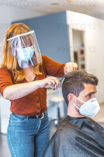 Hairdressers after the Coronavirus pandemic. Hairdresser with face mask and protective screen