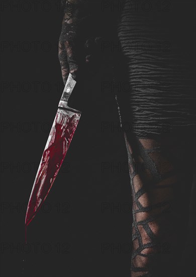 Hand with black lace glove holds bloodstained knife next to woman's leg