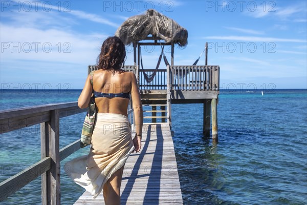 A young girl in a bikini walking to a wooden construction of the Caribbean Sea on Roatan Island. Honduras