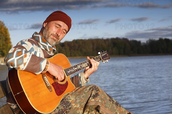 Man playing guitar on a jetty by the lake