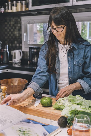 Mid-adult woman reading recipe while preparing food in the kitchen. Vertical shot