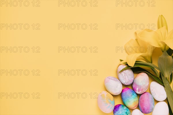 Fresh lily flowers with colorful easter eggs corner yellow background