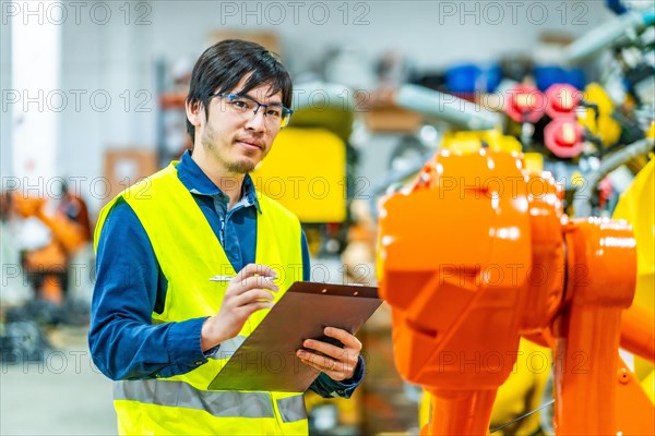 Young japanese engineer on duty controlling an industrial production line of robotic arms