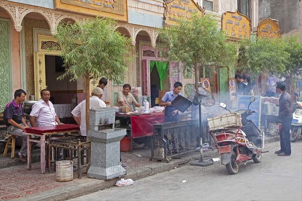 Uyghur men eating grilled meat outdoors at small traditional restaurant in the city Kashgar