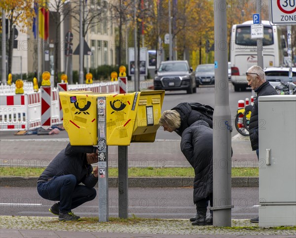 Tourists marvelling at and examining a yellow letterbox by the roadside
