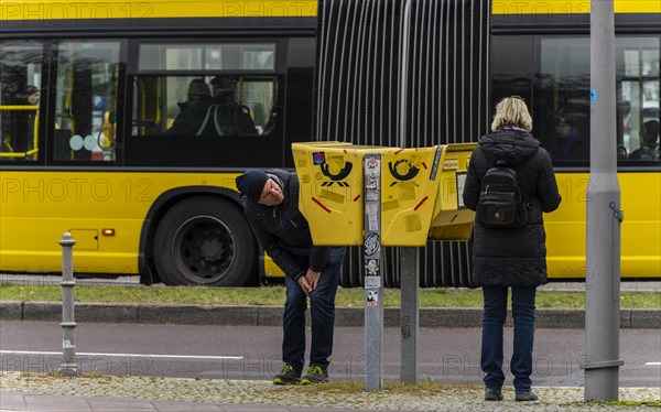 Tourists marvelling at and examining a yellow letterbox by the roadside