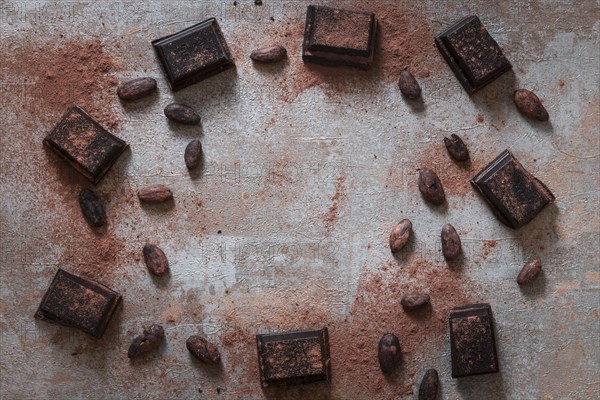 Overhead view broken chocolate bas with cocoa powder raw beans