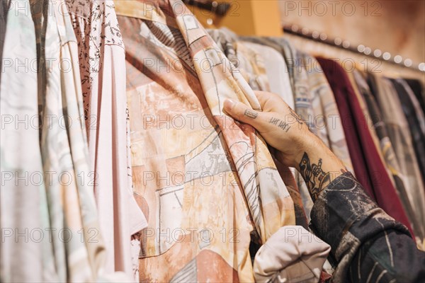 Close up male customer s hand choosing shirt hanging rail shop