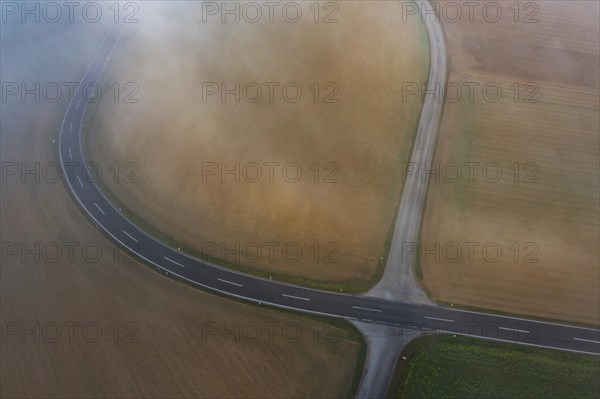 Drone view of a rural landscape shrouded in dense morning fog with a road junction near Prambachkirchen