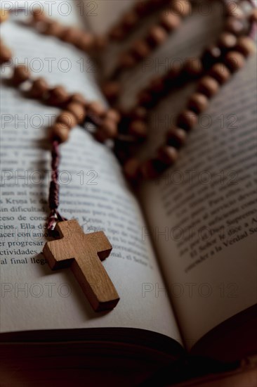 Rosary with a wooden christian cross on a bible with open pages