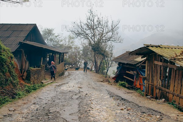 Dreamy scenery of a muddy road and native house on a foggy winter day
