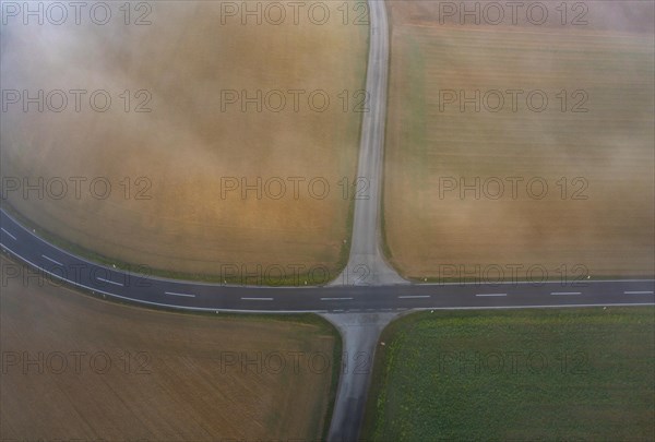 Drone view of a rural landscape shrouded in dense morning fog with a road junction near Prambachkirchen