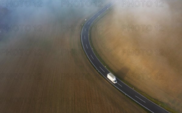 Drone view of a rural landscape shrouded in dense morning fog with a country road near Prambachkirchen