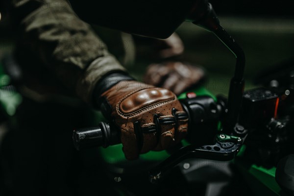 A motorcyclist in brown leather gloves sits on a motorcycle