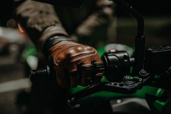 A motorcyclist in brown leather gloves sits on a motorcycle