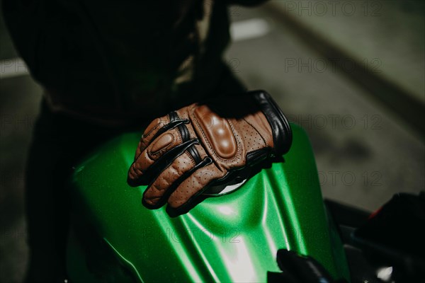A brown leather motorcyclist glove lies on the tank of a green motorcycle
