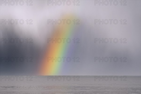 Colourful rainbow over sea water and approaching snow shower along the North Sea coast in winter