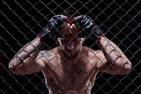 Dramatic image of a mixed martial arts fighter standing in an octagon cage. The concept of sports
