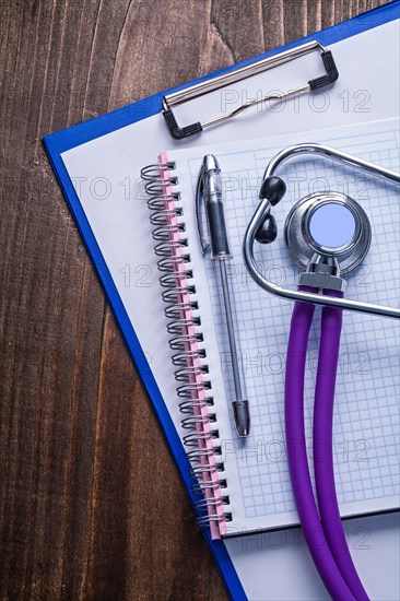 Medical stethoscope with purple tubes on clipboard with biros and vintage wooden board