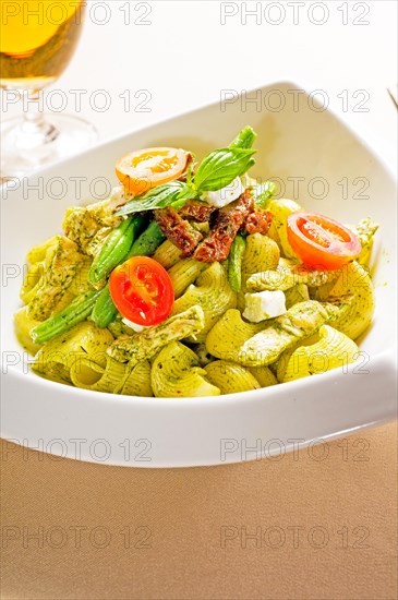 Fresh lumaconi pasta and pesto sauce with vegetables and sundried tomatoes