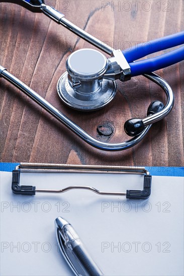 Clipboard with paper sheet and biros Stethoscope on vintage wooden board