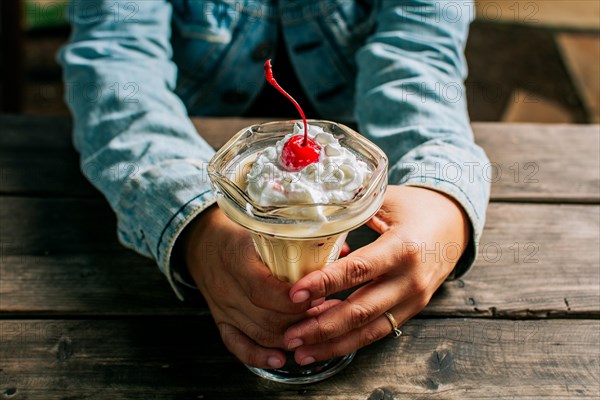 Female hand holding cherry milkshake on wooden table. Person holding cherry smoothie over wooden table