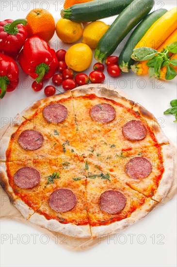 Italian original thin crust pepperoni pizza with fresh vegetables on background