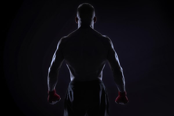 Kickboxer in red bandages posing on a blue background. Back view. The concept of mixed martial arts. MMA