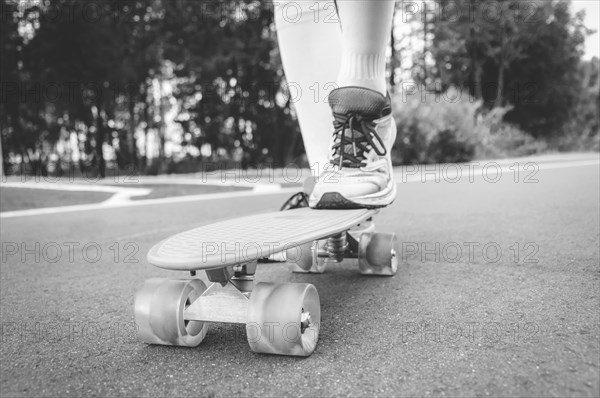 Images of a leg standing on a skateboard. Sunny evening in the park. Skateboarding concept.