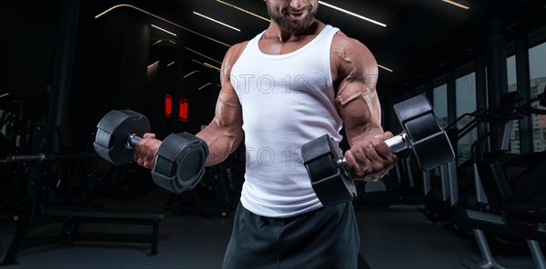 Portrait of a man in a white T-shirt exercising in the gym with dumbbells. Biceps pumping. Fitness and bodybuilding concept.