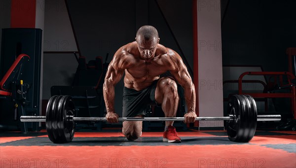 Athlete is standing on his knee and near the bar in the gym and is preparing to make a deadlift.