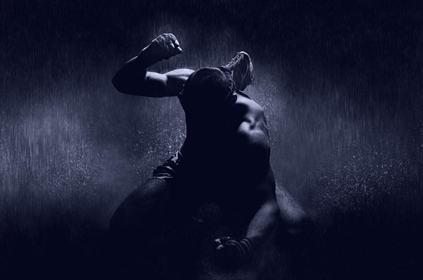 Thai boxer in the rain and under a blue spotlight. Mongkhon. The concept of victory in competitions
