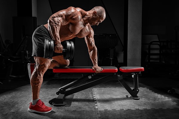 Muscular man pulls a dumbbell towards his stomach. Bodybuilding and powerlifting concept.