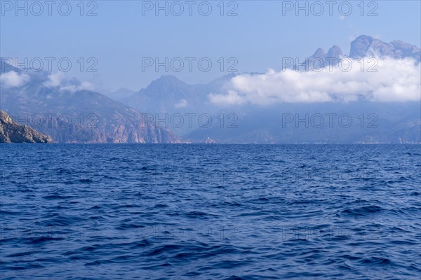 A calm seascape with mountains in the background and clouds in the sky