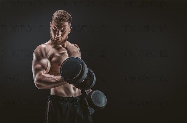 Young muscular guy pumping biceps with dumbbells. Concentrated flexion. Fitness and nutrition concept.