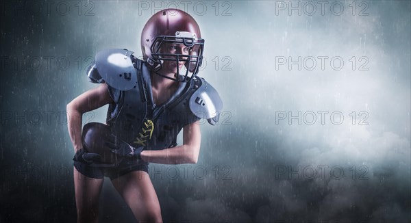 Image of a girl in the uniform of an American football team player. She runs with the ball against the background of light spots. Sports concept. Shoulders pads.